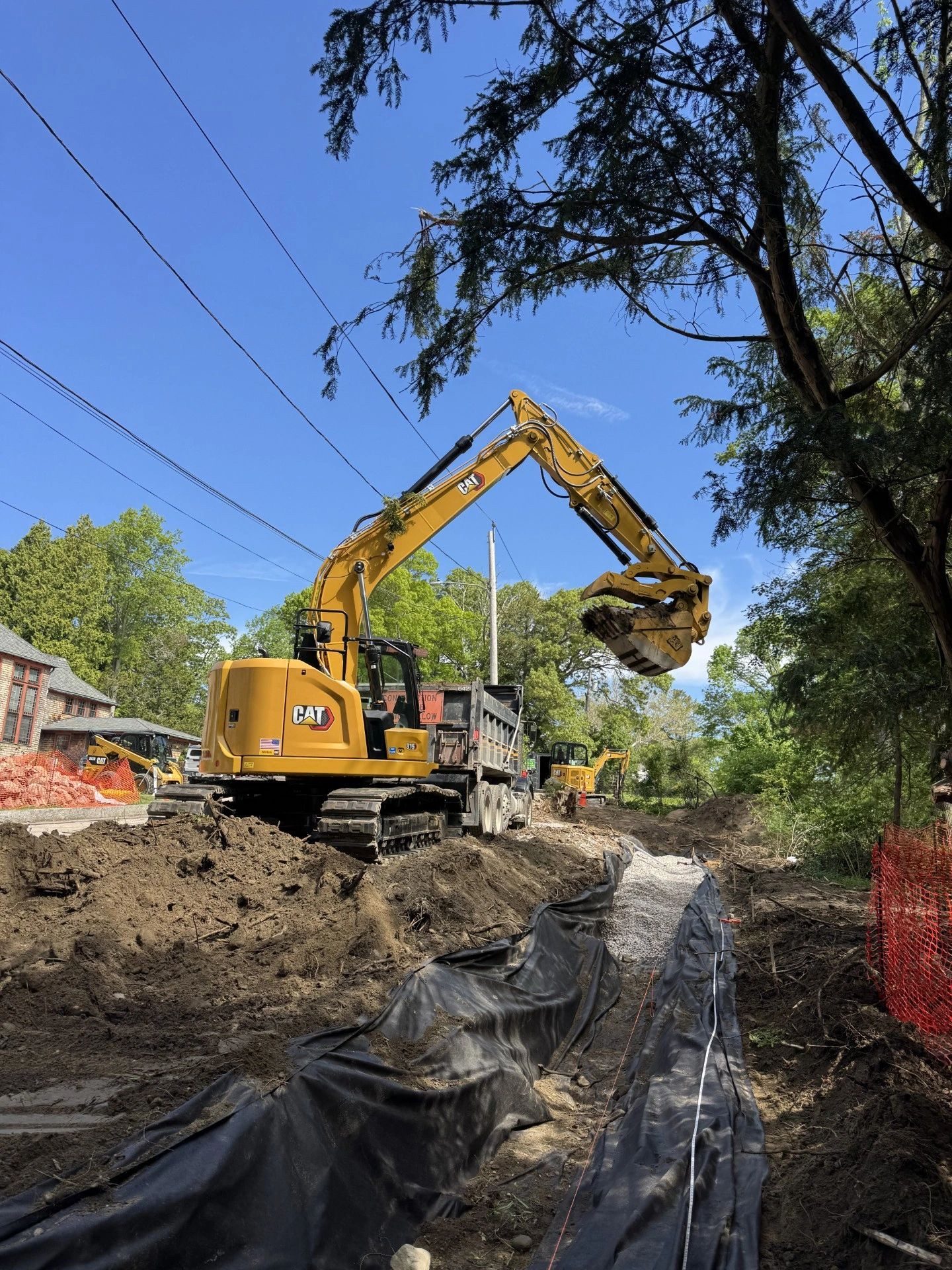 Excavator loading a dump truck during a roadside utility installation