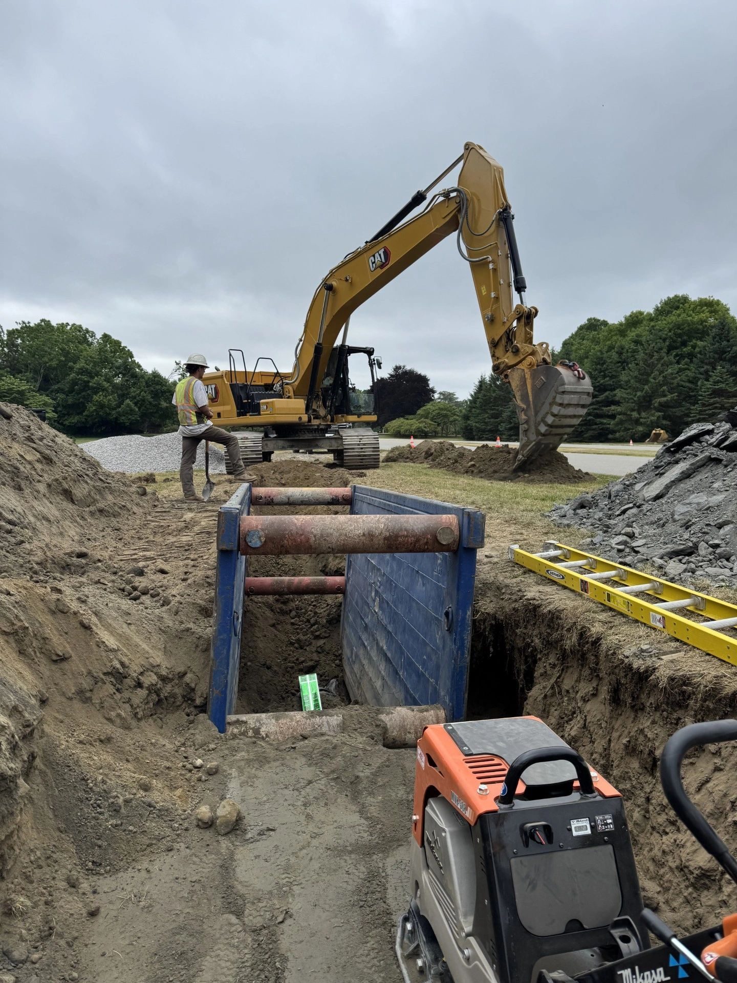True North Civil crew working a shored utility trench with a compactor and excavator